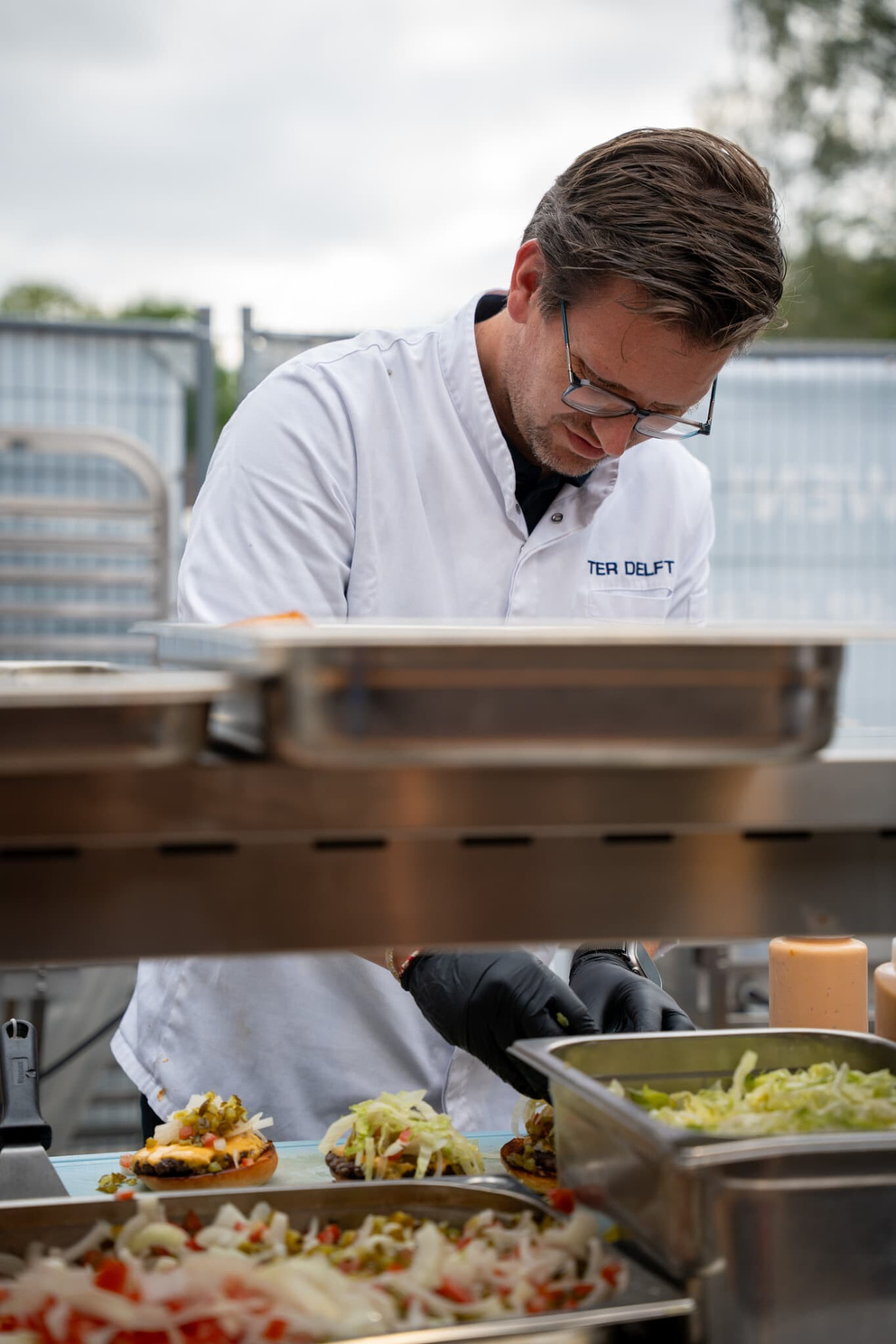 Een kok bereidt kleurrijke gerechten in een professionele keuken met verschillende ingredi&euml;nten op de achtergrond.