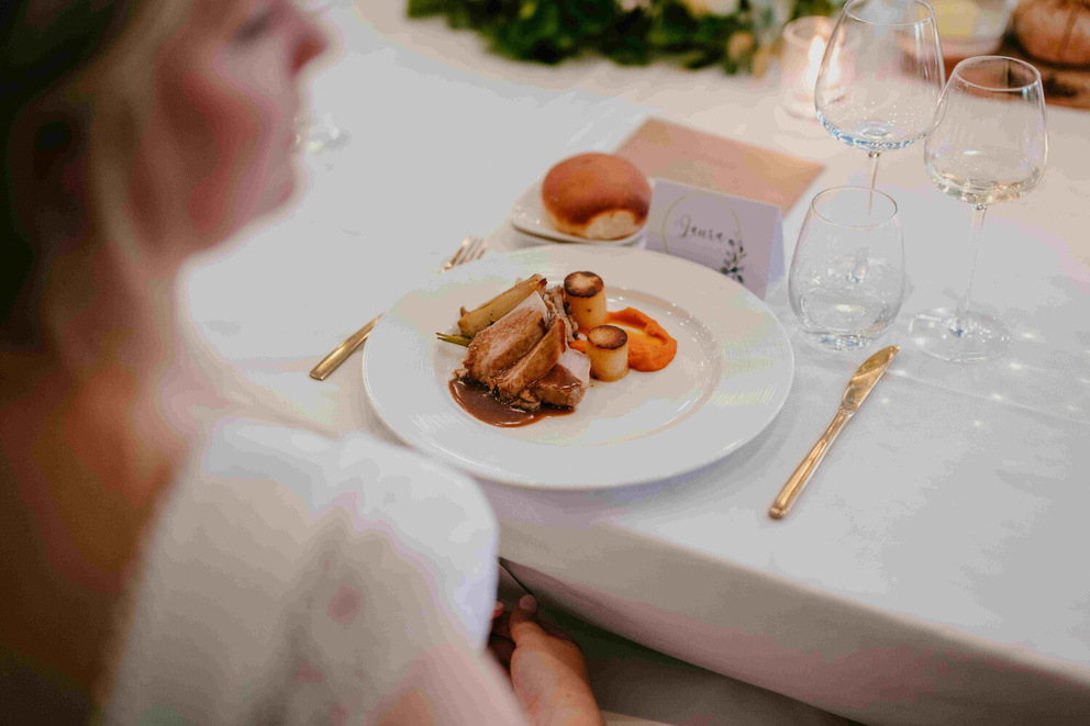 Een elegant diner met gebraad, groenten en een bolletje brood, geserveerd met glazen en een naamkaartje op de tafel.