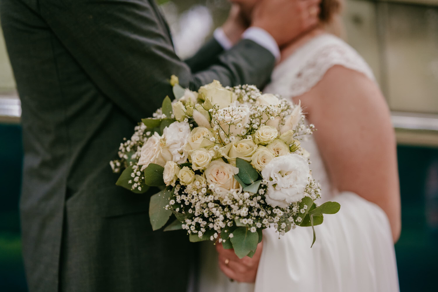 Een bruid in een witte jurk houdt een boeket met witte en crèmekleurige bloemen vast, terwijl ze intiem met haar partner is.