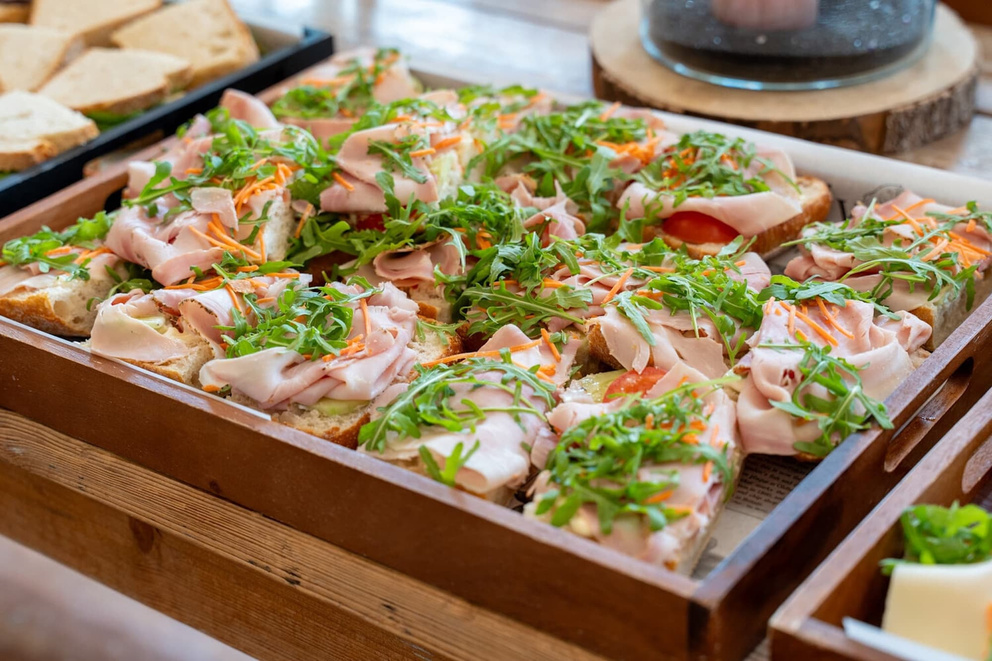 Een houten schaal met belegde sandwiches, rijkelijk gegarneerd met ham, groenten en verse kruiden.