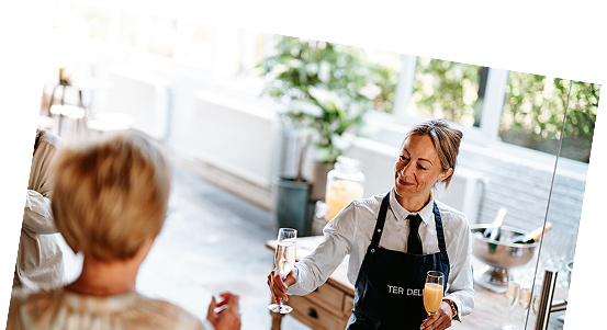 Een serveerster schenkt champagne in een moderne horecagelegenheid, met een glimlach naar een gast.