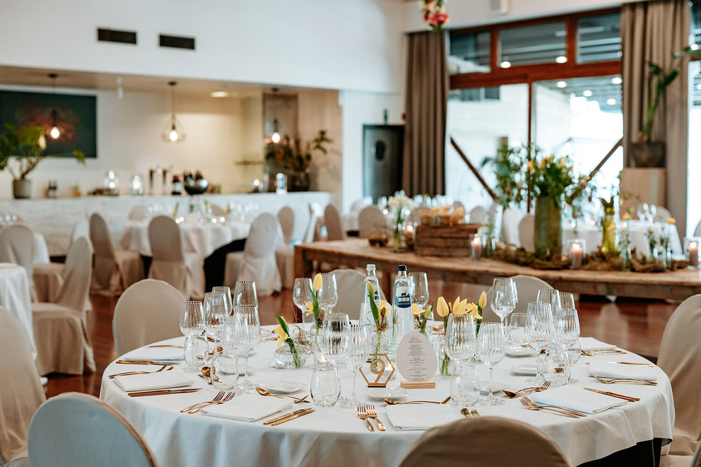 Elegant gedekte tafels met glazen en bloemen in een sfeervolle ruimte, perfect voor een feestelijke gelegenheid.