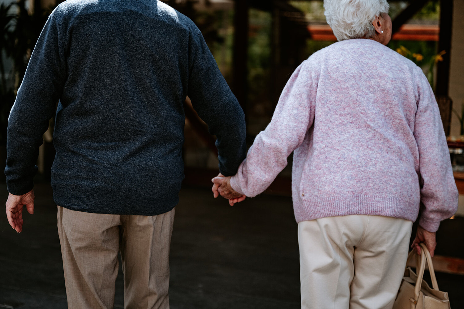 Een ouder echtpaar houdt hand in hand elkaar vast, terwijl ze samen een rustige wandeling maken.