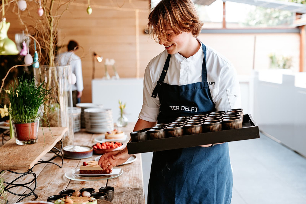 Medewerker van Hof ter Delft draagt een plateau met desserts langs het buffet