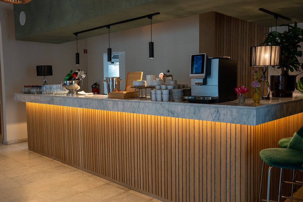 Moderne bar met marmeren toog, houten panelen, verlichting en een assortiment dranken en glazen.