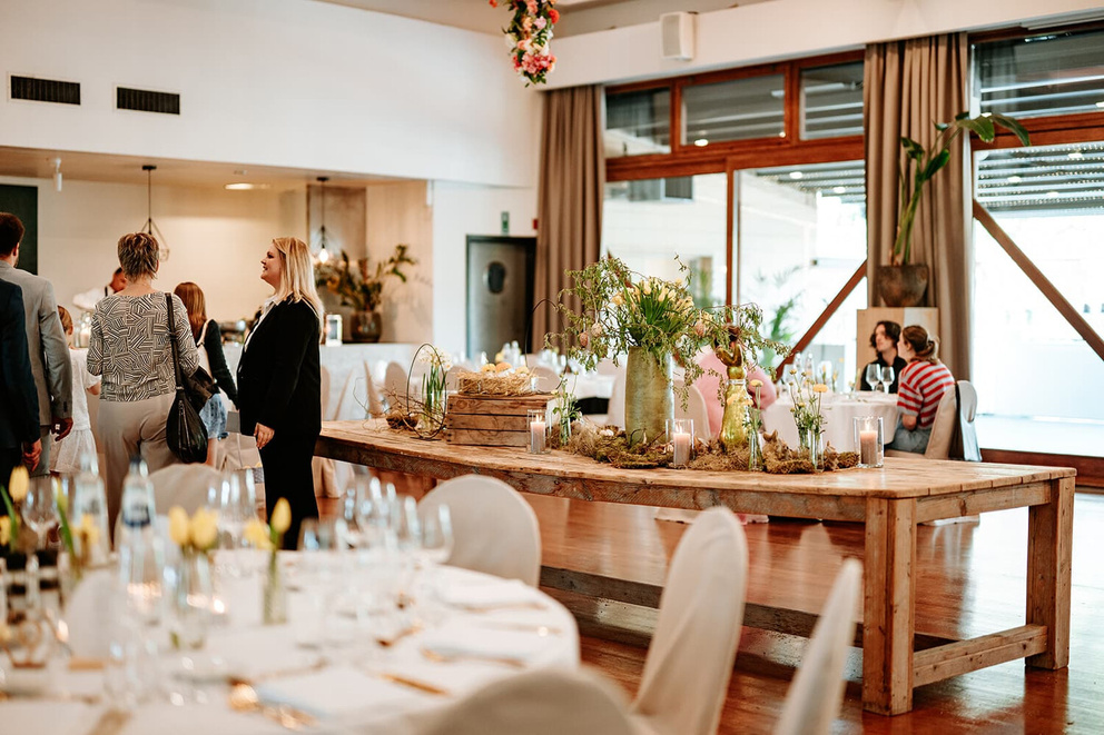 Luxe eetzaal met lange houten tafel, decoraties en gasten in gesprek, sfeervol ingericht voor een feest.