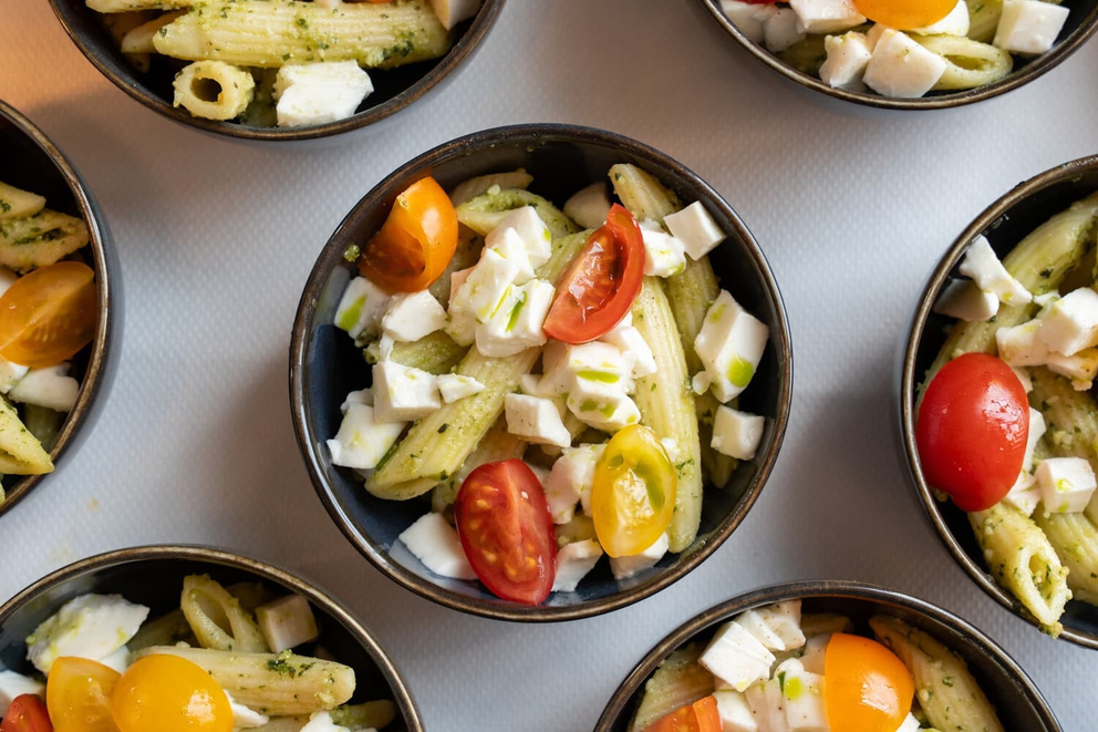 Pasta met pesto, cherrytomaatjes en blokjes feta in zwarte kommen.