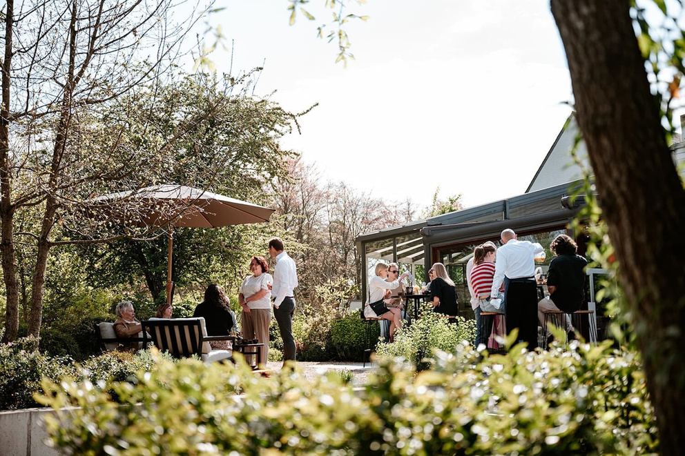 Mensen socializen op een zonnige dag in een tuin met planten en een parasol.