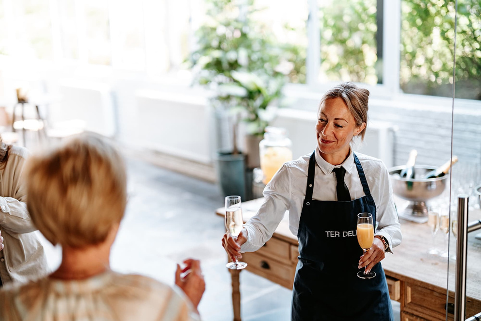 Medewerker van Hof ter Delft serveert glazen cava en jus aan een gast