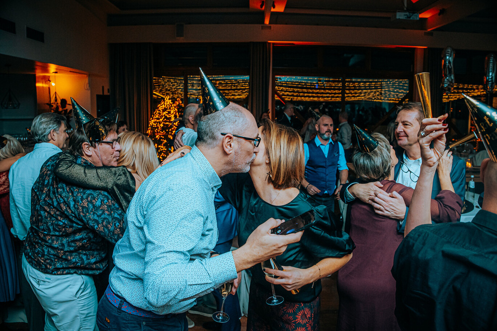 Mensen vieren een feestje met feesthoedjes, proosten en dansen in een sfeervolle ruimte.